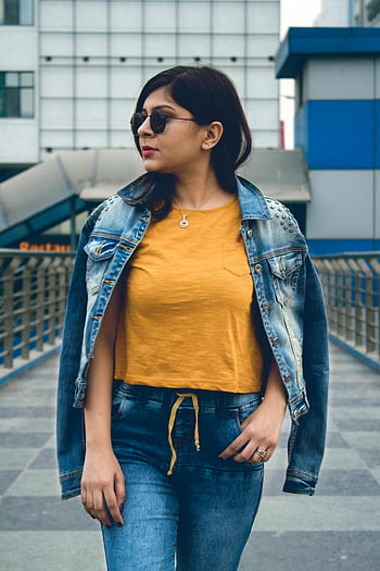 Vrouw draagt ​​spijkerjas, stijlvolle vrouw, zonnebril, zelfverzekerd poseren, buitenshuis, gele top, spijkerbroek, stedelijke omgeving, zelfverzekerde pose, Casual mode, Street Style