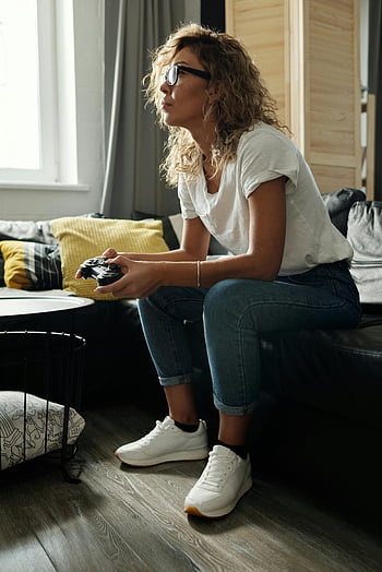 Vrouw die op de bank zit, videogamesessie, gezellige bank, gerichte vrouw, ontspannen vrouw, Home Gaming, Vrijetijdsoutfit, woonkamer setting, binnenweg, comfortabele schoenen, Moderne leefruimte