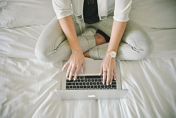 Macbook Pro, Person, die Laptop verwendet, Arbeiten am Bett, Casual Work Setup, Innenministerium, Bequemer Arbeitsbereich, Laptop auf Schoß, weiße Bettwäsche, Moderne Technologie, Produktivität, Heimarbeit