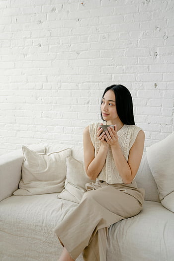 アジアの女性、 飲み物、 ソファーに座っていた、 若い女性、 コーヒーを楽しんでいます、 居心地の良いソファ、 平穏な瞬間、 家に、 白いレンガの壁、 快適な衣装、 屋内設定