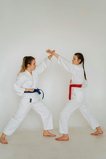 žena trénuje karate, dvě ženy trénují, uniformy pro karate, Světlé studio, bojová umění, sparing session, Karate praxe, ženy bojových umění, Bílá karate gi, červený pás, modrý pás