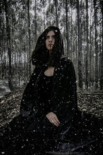 woman in black hoodie, snowy winter forest, dark cloak, mysterious woman, winter scene, forest setting, black clothing, hooded figure, snowfall, atmospheric photo, dark attire