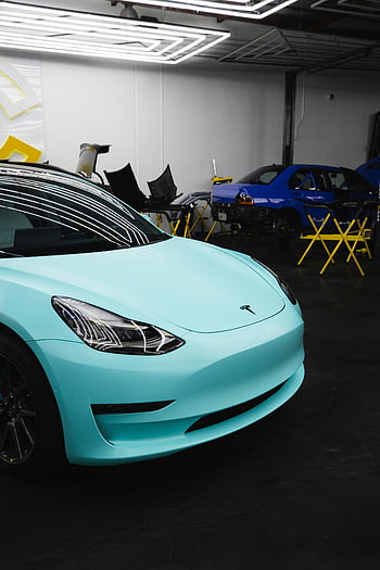 Blue Tesla car, turquoise Tesla, modern Tesla, parked Tesla, garage interior, overhead lights, electric vehicle, Tesla Model 3, car maintenance, garage setup, Tesla showroom