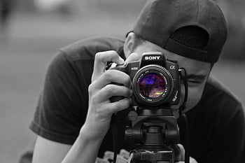 man holding DSLR camera, close-up photographer, focusing camera, tripod outdoors, creativity, Sony camera, outdoor photography, photographer working, camera lens, black and white photo, photography equipment