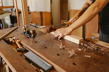 woodworker, cutting, wooden plank, hacksaw, skilled carpenter, handsaw, timber, workbench, well-equipped workshop, carpentry tools, woodworking