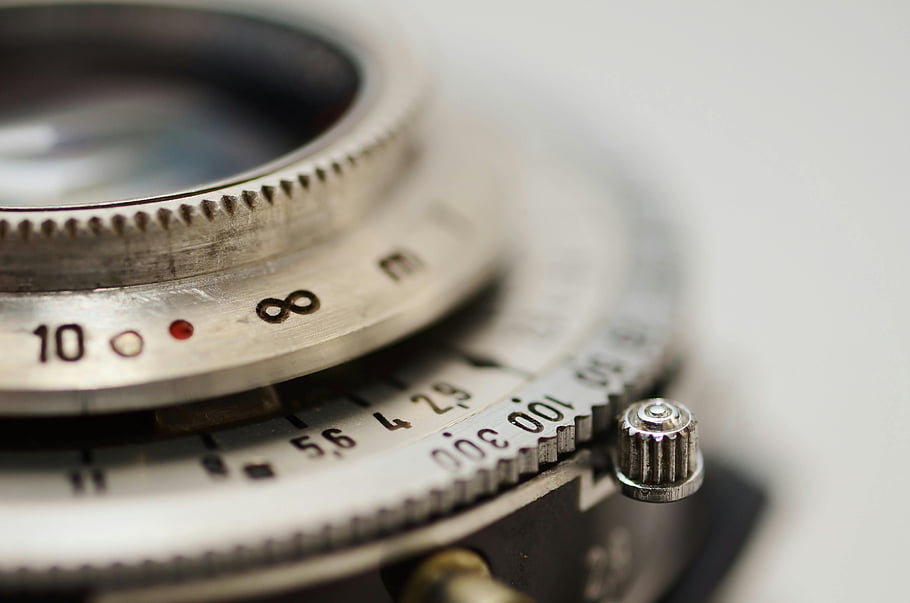 vintage camera lens, aperture settings, focus dial, macro shot, silver-colored gauge, detailed photography, camera equipment, close-up image, photographic lens, aperture control, focus adjustment