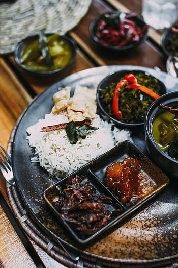 Asian cuisine, rice dish, side dishes, rustic table, appetizing meal, white rice, curry sides, vegetable sides, traditional food, black plate, wooden table