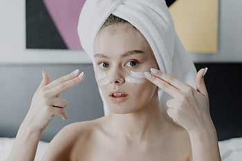 mujer, toalla blanca, rutina de cuidado de la piel, Aplicando crema facial, mujer joven, toalla en la cabeza, rutina de belleza, cuidado facial, protección de la piel, autocuidado, tratamiento de belleza