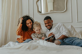 family reading, book on bed, joyful family, bonding over book, home setting, parents and child, family time, cozy bedroom, reading together, family activity, happy family