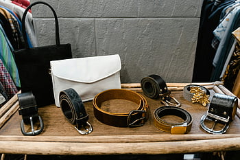 černé kožené opasky, hnědý dřevěný stůl, stylové pásky, kabelky, dřevěný stojan, Módní butik, různé pásy, kožené doplňky, butikový displej, módní doplňky, kožené kabelky