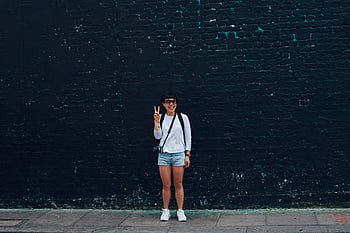 donna, Shorts di denim blu, muro di mattoni neri, sorridente, occhiali da sole, segno di pace, in posa, muro di mattoni, Abbigliamento casual, stile di strada, sfondo urbano