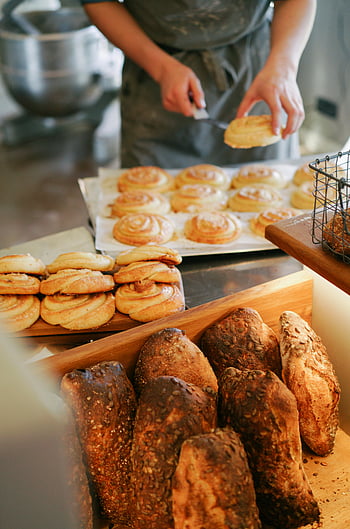 Pain complet, plateau en bois, brioches à la cannelle, pain de campagne, boulangerie artisanale, pain frais, boulangerie, présentoir à pain, pain artisanal, scène de boulangerie, assortiment de pain