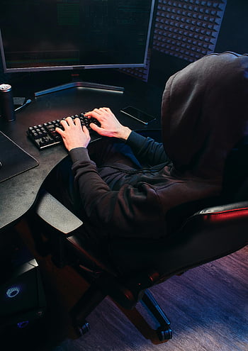 Hrozby kybernetické bezpečnosti, postava s kapucí, psaní na klávesnici, zpětný pohled, tajemná osoba, počítačový stůl, temná místnost, kybernetická bezpečnost, hacker, online zabezpečení, technologie