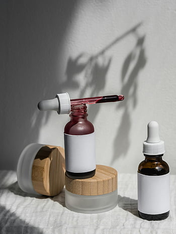 beauty products, skincare products, minimalist display, natural light, artistic shadows, close-up shot, dropper bottles, wooden containers, white labels, aesthetic presentation, product photography