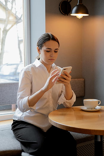 woman using mobile phone, smartphone, cafe, coffee, white shirt, table, indoor, casual setting, focused, technology, lifestyle