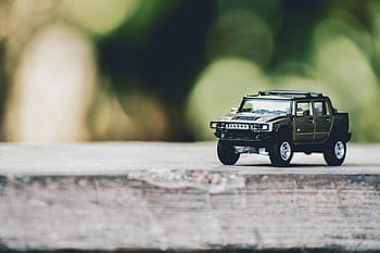miniature toy truck, selective focus photography, gray Hummer truck, outdoor surface, blurred natural background, close-up miniature, toy vehicle, outdoor photography, natural backdrop, toy car, miniature photography