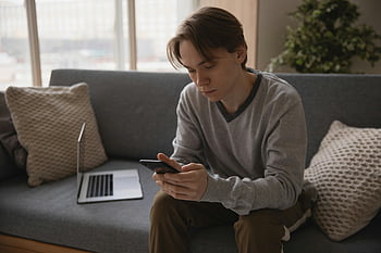 człowiek za pomocą smartfona, młody człowiek, siedząc na kanapie, smartfon, laptop w pobliżu, nowoczesna technologia, wewnątrz, Zwyczajny outfit, salon, ustawienie domowe, wykorzystanie technologii