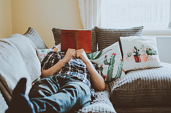 person laying on sofa, reading book, relaxing at home, lying on sofa, book, cushions, cozy living room, comfortable sofa, home leisure, indoor relaxation, casual reading
