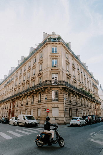 classic building, urban intersection, parked cars, person on scooter, city street, corner building, urban scene, street view, classic architecture, cityscape, urban environment