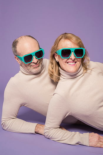 senior couple, matching sweaters, sunglasses, purple background, studio, playful pose, happy couple, couple outfit, senior fashion, studio photography, couple style