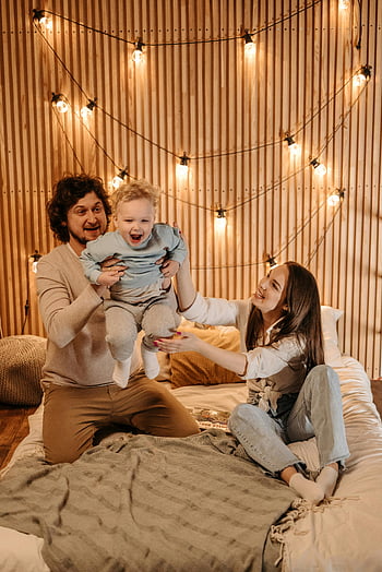 happy family, playing together, bed, cozy room, string lights, joyful bonding, fun moments, togetherness, family time, indoor play, warm atmosphere