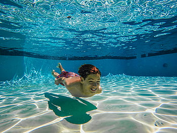 shirtless kid, swimming underwater, brightly lit, swimming pool, boy enjoying, underwater swim, pool floor, water surface, light reflections, swimwear, underwater photography