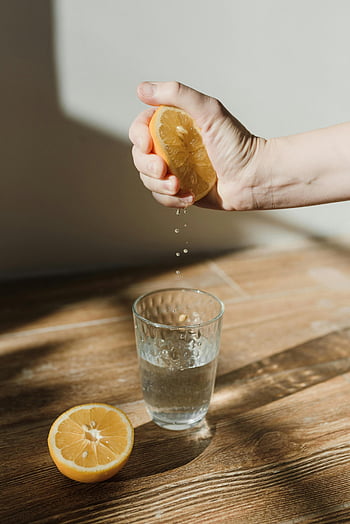 Stisknutí citronu, sklenice vody, dřevěný povrch, čerstvý citron, mačkání rukou, citronová šťáva, osvěžující nápoj, citrusové ovoce, zdravý nápoj, přírodní ingredience, citronová voda