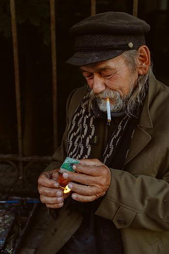 elderly man, smoking cigarette, lighting match, urban environment, outdoor scene, ethnic man, street photo, cigarette smoker, match lighting, urban street, elderly smoker