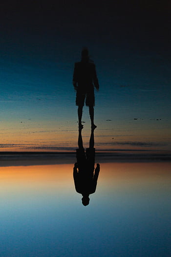 sunset reflection, person silhouette, water reflection, beach scene, twilight sky, human figure, mirrored image, calm water, evening light, natural beauty, serene moment