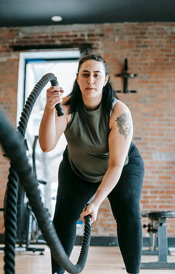 woman exercising, battle ropes, gym workout, endurance training, strength training, determined woman, fitness, gym exercise, workout routine, indoor gym, fitness equipment