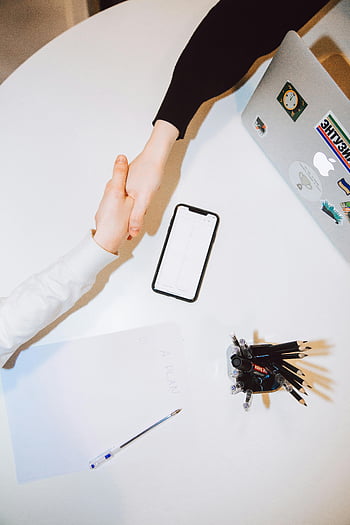 Handschlag, modernes Büro, Smartphone, Laptop, Schreibtisch, Geschäftstreffen, professionelle Interaktion, Büroeinstellung, Zusammenarbeit, Arbeitsumgebung, Technologie im Büro