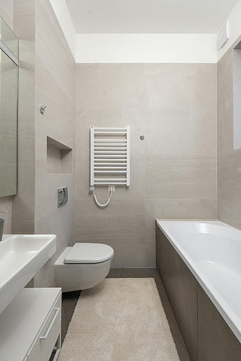 minimalistinen kylpyhuone, valkoinen keraaminen kylpyamme, nykyaikainen kylpyhuone, tyylikäs muotoilu, kylpyamme, pesuallas, WC, moderni kylpyhuone, beige laatat, valkoiset kalusteet, kylpyhuoneen sisustus