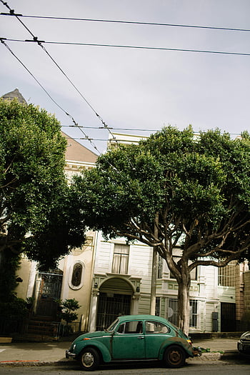 voiture rétro, rue de la ville, voiture verte classique, arbres luxuriants, rue urbaine, architecture historique, véhicule d'époque, voiture garée, scène de rue, paysage urbain, coléoptère vert