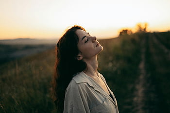 美しい若い女性、 牧草地に立っています、 目を閉じて、 穏やかな女性、 暖かい夕日、 フィールド、 頭を傾けた、 夕日を味わう、 平穏な瞬間、 自然シーン、 屋外の静けさ