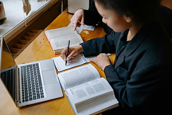 students studying, taking notes, books, laptop, wooden desk, indoor study, academic work, focused learning, educational environment, study session, note-taking