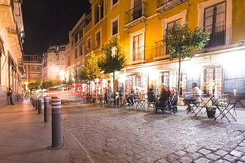 Pranzo europeo, Scena notturna, caffè illuminati, strada di mattoni, tavoli e sedie, Street vivace, pedoni sfocati, posti a sedere all'aperto, vita notturna urbana, Atmosfera accogliente, caffè di strada