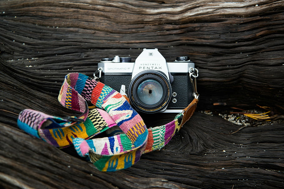 Pentax camera, gray and black, vibrant strap, classic camera, natural driftwood, Honeywell Pentax, Spectromatic SP, colorful strap, vintage camera, outdoor photography, driftwood background