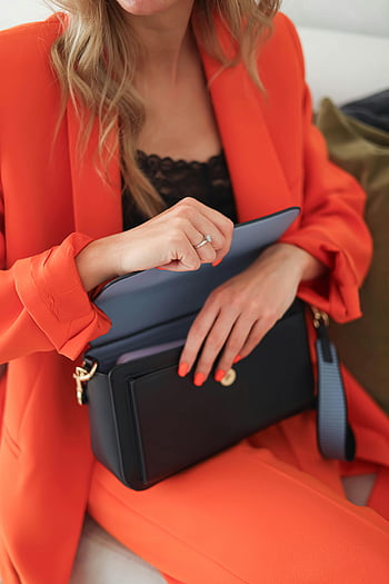 žena v červeném obleku, černá kožená kabelka, Oranžový oblek, Stylová kabelka, módní žena, Vnitřní móda, zapínání kabelky, elegantní outfit, moderní móda, Vnitřní nastavení, styl doplňků