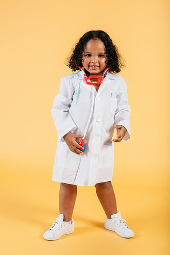 smiling black girl, medical costume, doctor's coat, toy equipment, yellow background, studio photo, happy child, bright yellow backdrop, medical play, children's costume, playful doctor