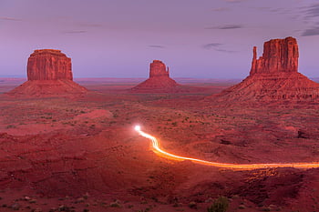 Monument Valley, sunset view, sandstone buttes, light trails, dramatic landscape, brown rock formation, vibrant sandstone, desert scenery, natural wonder, scenic route, Arizona landscape