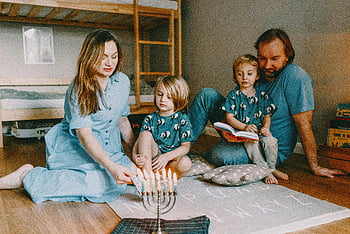 Rodina slaví Hanukkah, Osvětlení Menorah, Útulné domácí nastavení, Oslava Chanuky, rodinné sešlosti, židovský svátek, Slavnostní atmosféra, Domácí oslava, Rodinná tradice, svátek světel, Menorah osvětlení