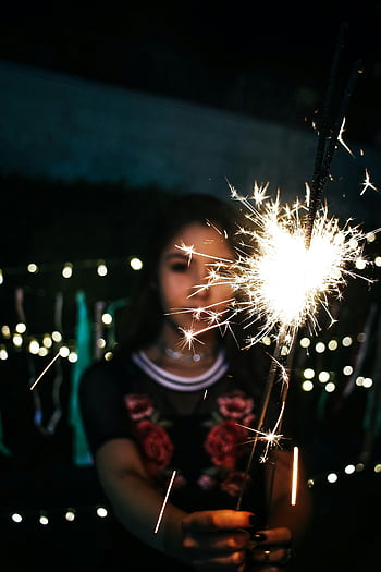 woman holding sparkler, nighttime sparkler, festive atmosphere, twinkling lights, bright sparkler, girl with sparkler, night scene, festive night, sparkler glow, outdoor celebration, night celebration