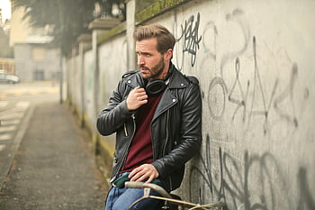 black full-zip biker jacket, fashionable man, black leather jacket, headphones, graffiti wall, outdoors, urban style, street fashion, casual look, modern man, leaning pose