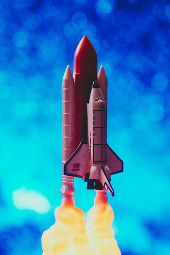 toy rocket ship, vibrant flames, bright blue bokeh, miniature rocket, launching rocket, toy space shuttle, United States, Atlantis, space exploration, toy flames, blue background