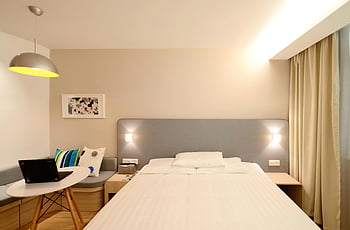 hotel room, minimalist interior, cozy lighting, contemporary design, laptop on table, modern decor, bed with pillows, wall art, hanging lamp, wooden floor, bedside table