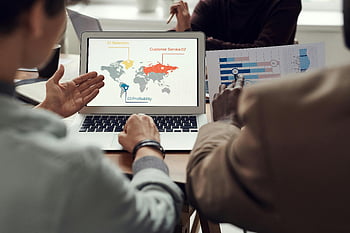 business strategy, team collaboration, global analytics, laptop display, man pointing, computer screen, business meeting, data analysis, office setting, professional discussion, strategy planning