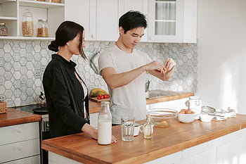 couple cooking, modern kitchen, Asian man, Caucasian woman, food preparation, kitchen setting, cooking together, kitchen counter, eggs, milk, bread