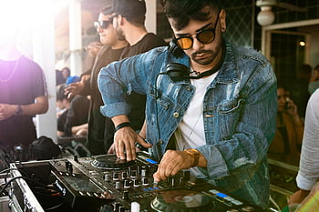 dj, giacca di jeans blu, controller dj nero, Evento diurno, folla, esibizione musicale, evento vibrante, DJ all'aperto, occhiali da sole, cuffie, piatto