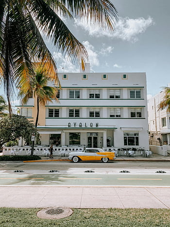 Art Deco hotel, Miami South Beach, classic yellow car, vintage style, palm trees, Avalon building, pastel colors, retro car, outdoor dining, sunny day, architectural design