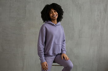 Smilende svart kvinne, hettegenser, høy stol, munter ung kvinne, avslappet lilla antrekk, Sitter innendørs, afro hår, lilla hettegenser, lilla antrekk, innendørs portrett, Uformell stil